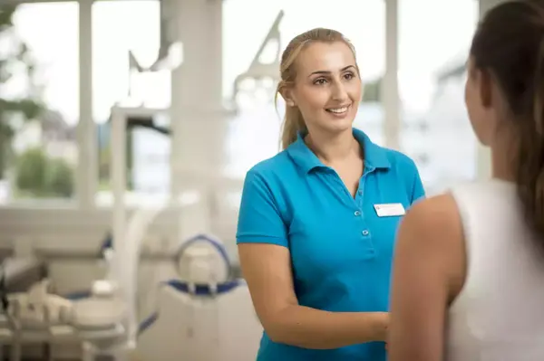 Freundliche Zahnärztin begrüßt Patientin in moderner Zahnarztpraxis mit heller Atmosphäre.