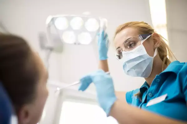 Zahnärztin mit Mundschutz und Handschuhen behandelt Patientin in moderner Zahnarztpraxis.