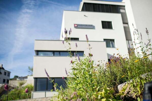 Modernes Gesundheitszentrum mit Blumenbeet und klarem Paracelsus-Schriftzug bei Sonnenschein.