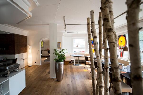 Modernes Restaurant mit Holzfußboden, Dekoration aus Birkenstämmen und großen Fenstern.